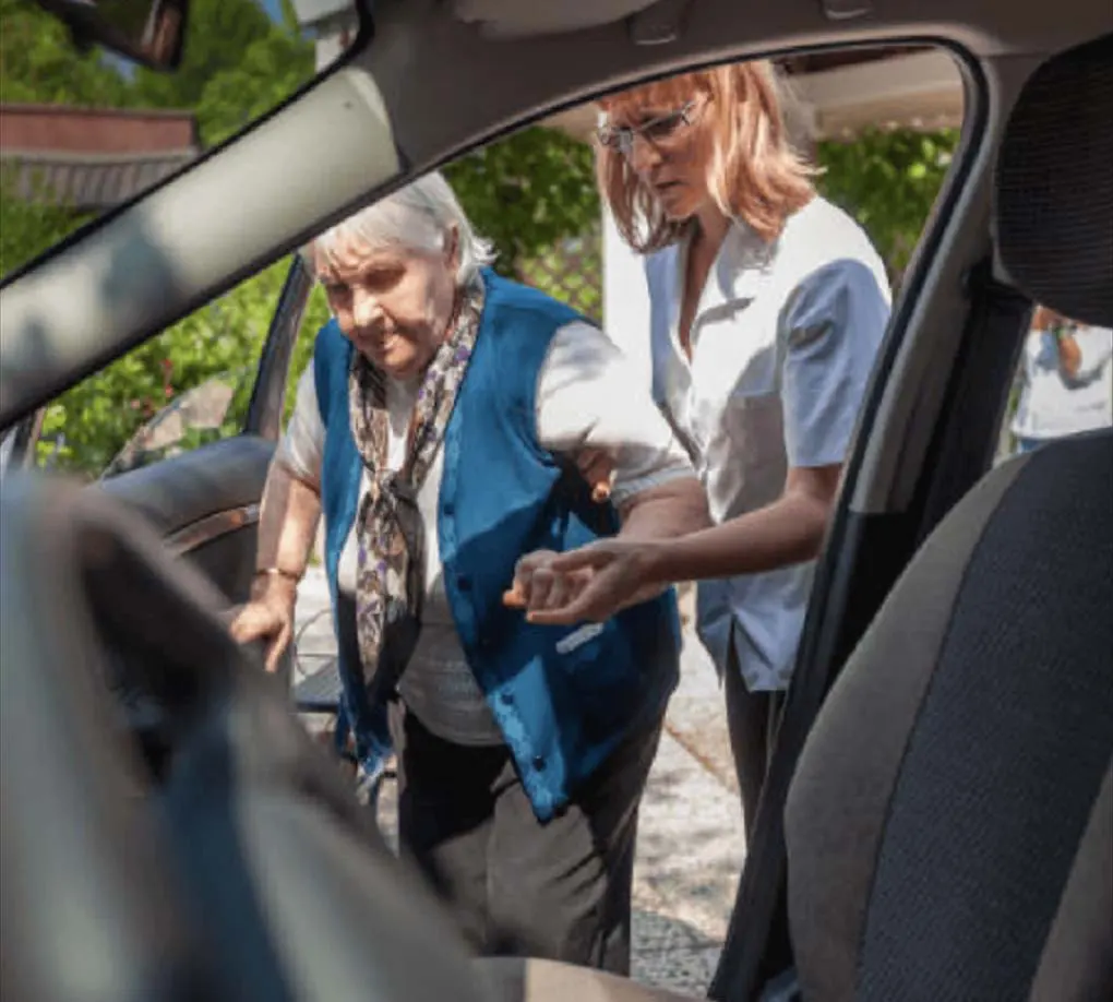 Senior woman being helped into a car by a no-cost transportation assistant